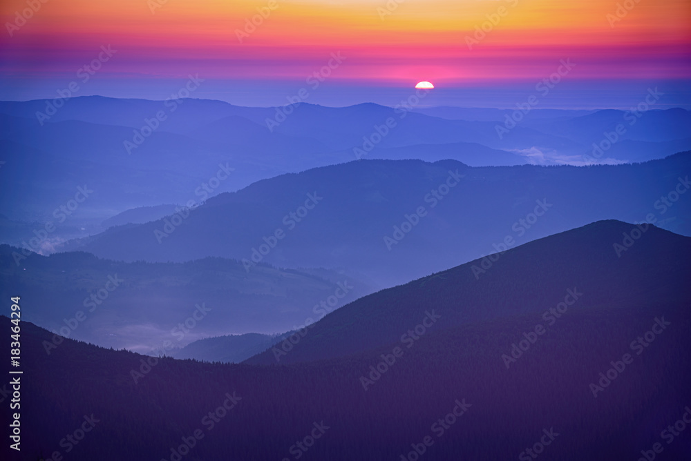 Amazing mountain landscape with colorful vivid sunrise on the bright sky over blue hills, natural outdoor travel background