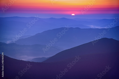 Amazing mountain landscape with colorful vivid sunrise on the bright sky over blue hills, natural outdoor travel background © Roxana
