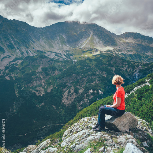 woman sits on the cliff and looks at the tops of mountains