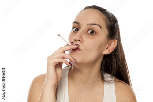 A young, pretty woman smokes a cigar on a white background