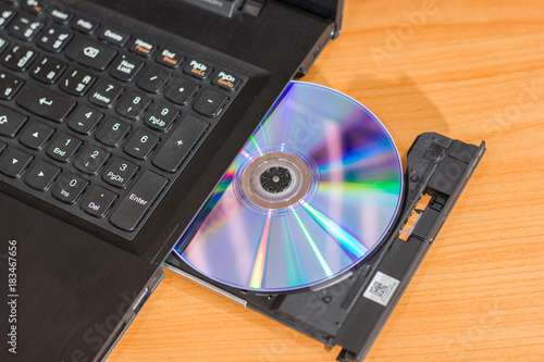 DVD ROM inserted in laptop computer on wooden texture background