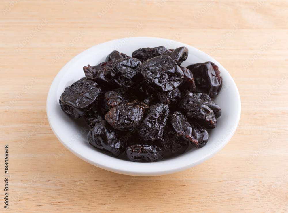 A portion of dried bing cherries in a small white bowl atop a wood table. A portion of dried bing cherries in a small white bowl atop a wood table.
