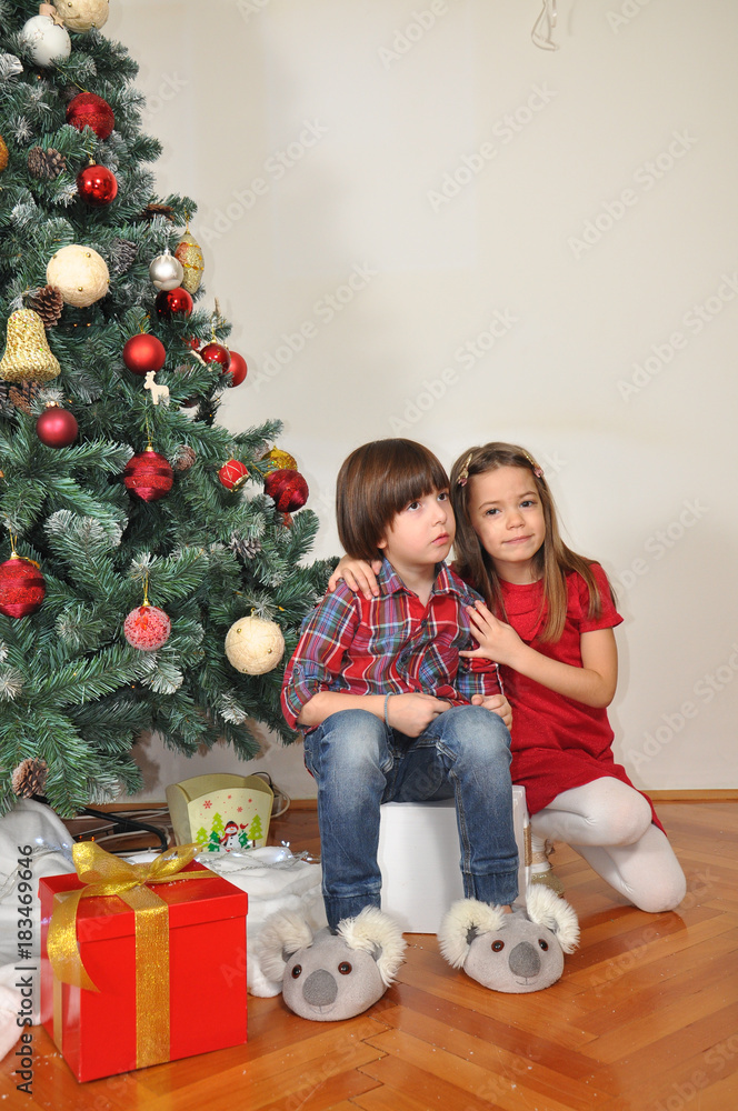 Boy and girl under a Christmas tree. Children talk and play under Christmas tree Boy and girl under a Christmas tree. Children talk and play under Christmas tree