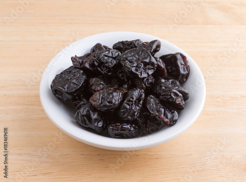 A portion of dried bing cherries in a small white bowl atop a wood table.