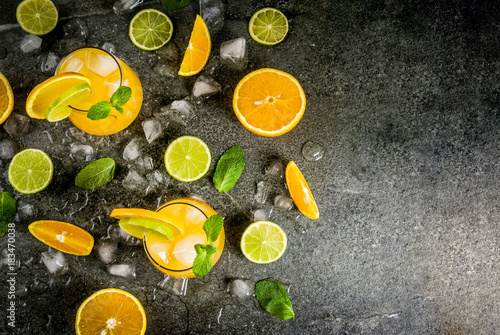 Fototapeta Naklejka Na Ścianę i Meble -  Vitamin summer refreshing drinks. Citrus punch with oranges and lime, with mint sprigs, chilled with ice. On black stone table, with ingredients, copy space top view