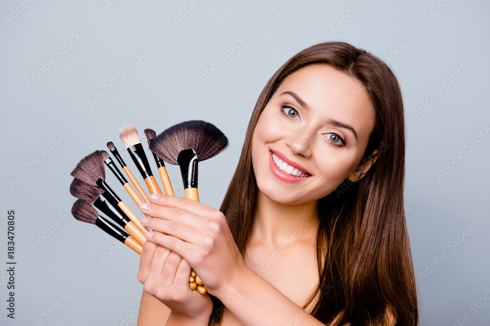 Close up photo of happy excited cute beautiful charming woman with beaming smile, she is holding a set of different brushes foe applying make up, isolated on grey background Close up photo of happy excited cute beautiful charming woman with beaming smile, she is holding a set of different brushes foe applying make up, isolated on grey background