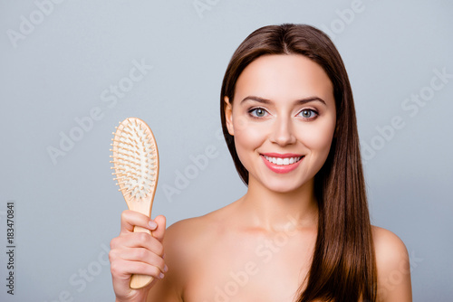 I don't lose hair anymore! Close up portrait of happy satisfied beautiful girl with shiny smile, she is showing a comb without hairs on it, isolated on grey background