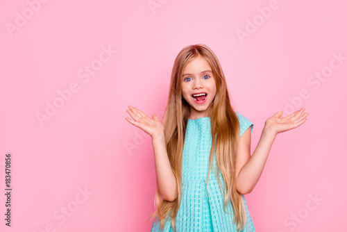 Happy beautiful surprised cute lovely charming small girl with open mouth and toothy smile, she is wearing blue dress, is gesturing with her hands, isolated on bright pink background, copyspace
