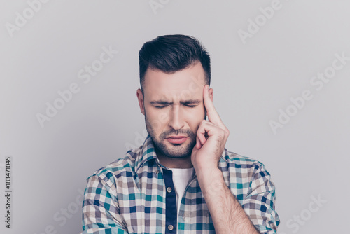 Stress and health care concept. Close up portrait of attractive guy with bristle, stubble having a headache, with close eyes touching his temple while standing over grey background