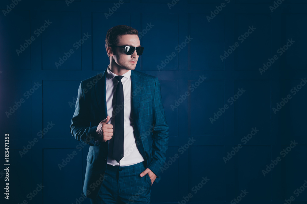Portrait of cool, elegant security chief holding hands in pocket and jacket, in black glasses, looking to the side over dark blue background Portrait of cool, elegant security chief holding hands in pocket and jacket, in black glasses, looking to the side over dark blue background