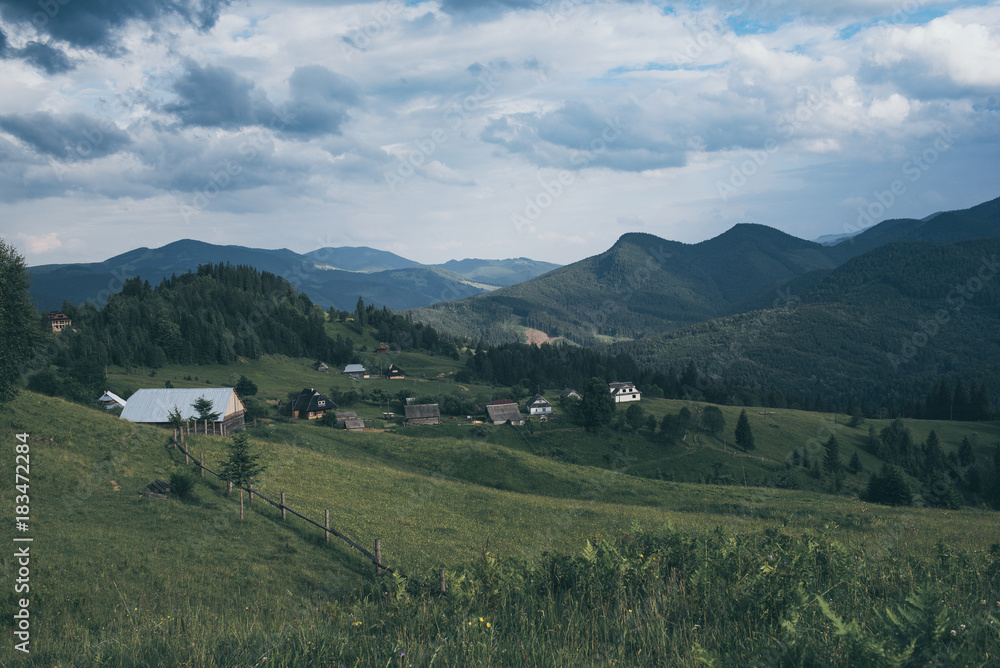 Fototapeta premium Carpathian mountains summer landscape with cloudy sky and village, natural summer travel background