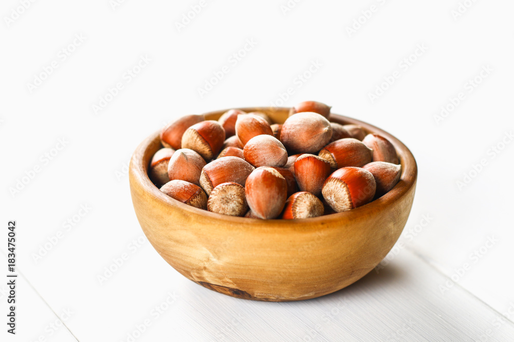 Hazelnut nuts in a wooden bowl on a white wooden table. Superfood. Hazelnut nuts in a wooden bowl on a white wooden table. Superfood.