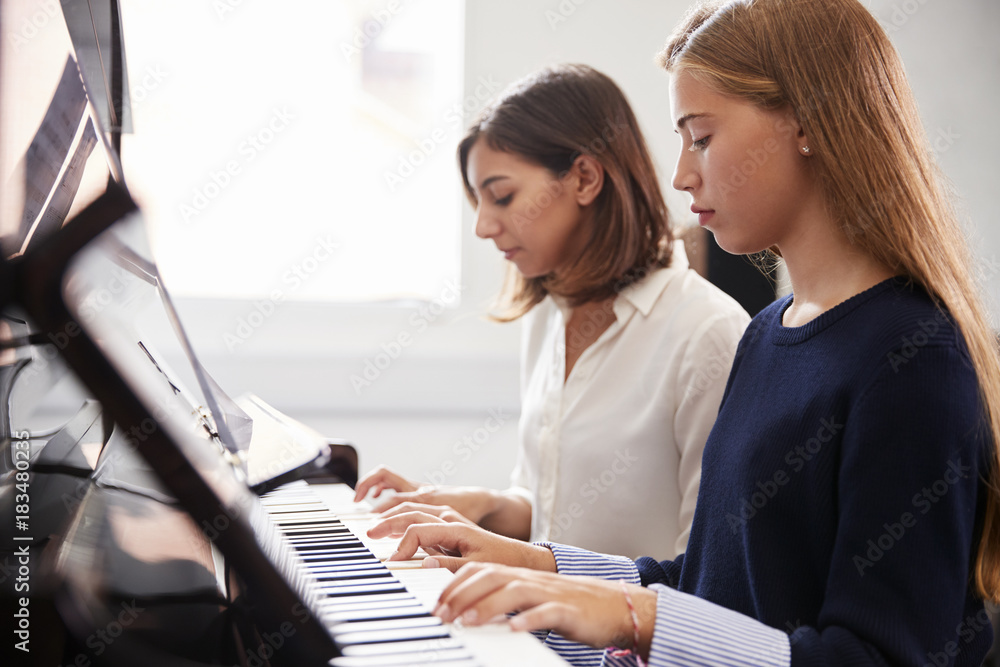 Fototapeta Female Pupil With Teacher Playing Piano In Music Lesson