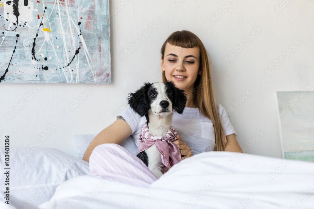 portrait of young woman with little puppy resting in bed in morning at home portrait of young woman with little puppy resting in bed in morning at home