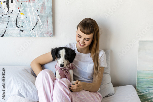 portrait of young woman with little puppy resting in bed in morning at home