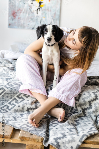 young woman hugging puppy while sitting on bed in morning at home