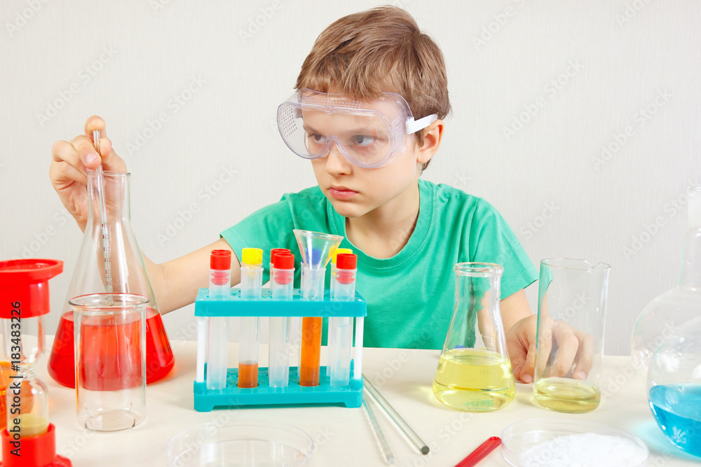 Young pensive boy in safety goggles doing chemical experiments in the laboratory Young pensive boy in safety goggles doing chemical experiments in the laboratory
