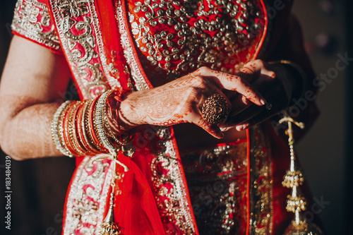 Tender hands of an Indian bride covered with henna tattoo while she dressed in red lehenga with golden embroidery