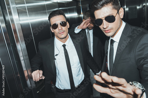 Bodyguards stopping paparazzi and celebrity covering face with hand in elevator