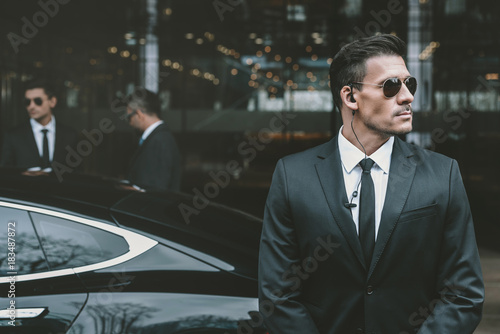 bodyguard standing at businessman car and reviewing territory
