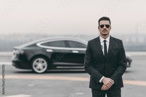 serious bodyguard standing with sunglasses and security earpiece on helipad photo
