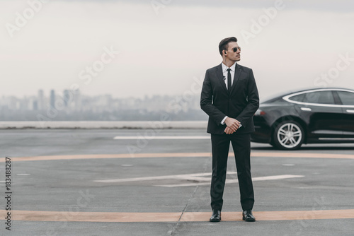 serious bodyguard standing with sunglasses and security earpiece on helipad and looking away