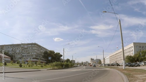 One car is driving down the street of the city between the buildings. Blue sky with white clouds.