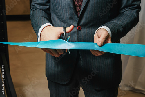 New business enterprise, opening, cutting a blue ribbon with scissors close-up.