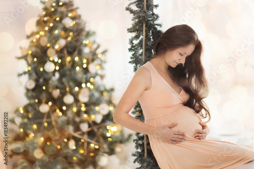 maternity woman near Christmas tree, golden