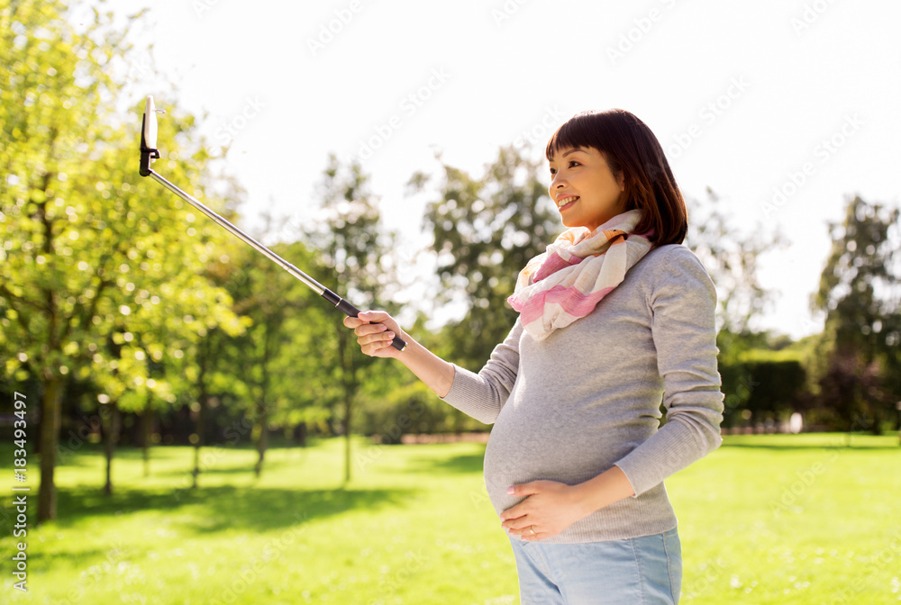 happy pregnant asian woman taking selfie at park happy pregnant asian woman taking selfie at park