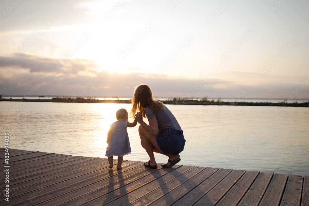 Mother and daughter walking on the wooden pier at sunny day, happy family on the beach Mother and daughter walking on the wooden pier at sunny day, happy family on the beach