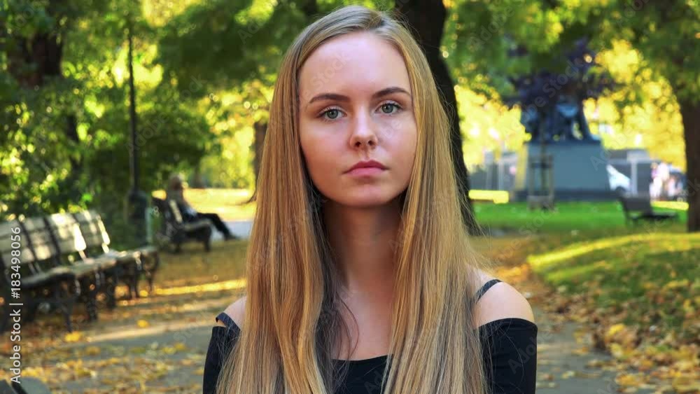 Young beautiful woman looks to camera with serious face in the park Young beautiful woman looks to camera with serious face in the park
