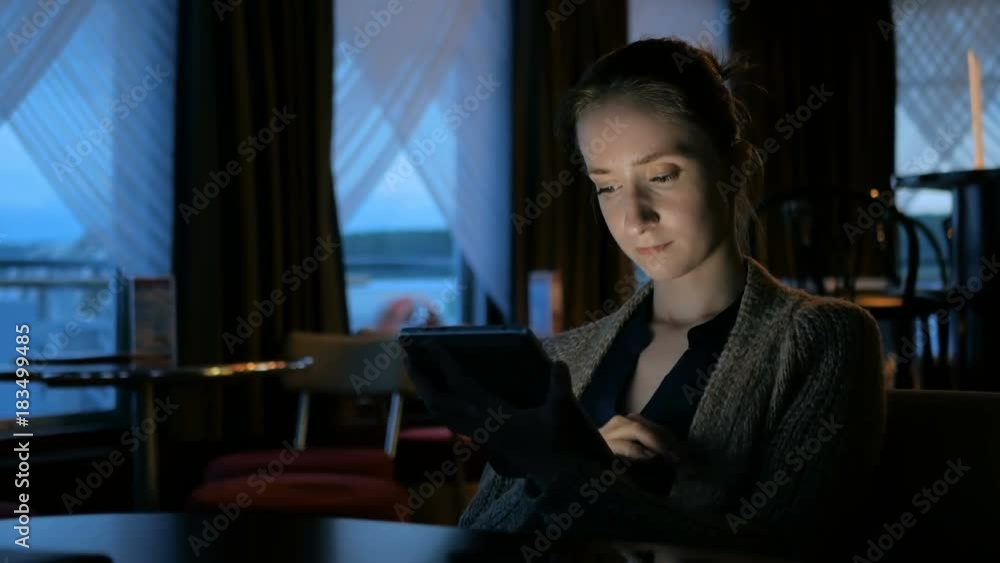 Woman using digital tablet computer device in cafe of cruise ship. Evening time, lowlight. Technology and entertainment concept Woman using digital tablet computer device in cafe of cruise ship. Evening time, lowlight. Technology and entertainment concept