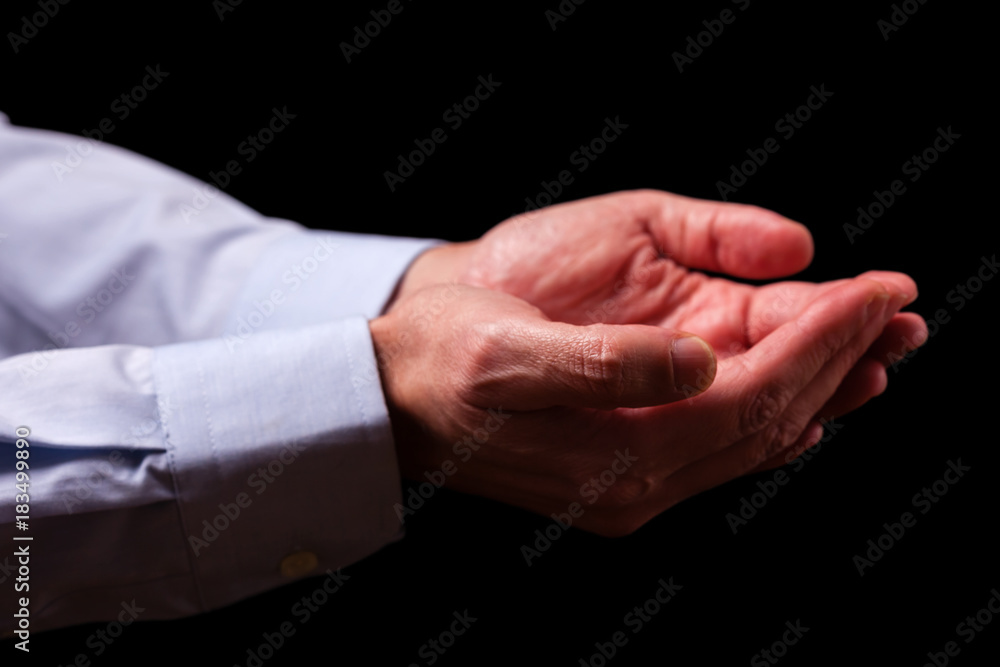 Mature male businessman hands together with empty palms up. Concept for man praying, prayer, faith, religion, religious, worship or giving, offering, begging, receiving. Black background.