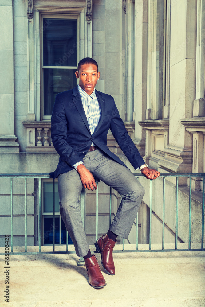 African American businessman working in New York. Wearing black blazer,  gray pants, brown leather shoes, a young guy sitting on railing in vintage  style office building, relaxing, . Stock Photo | Adobe Stock