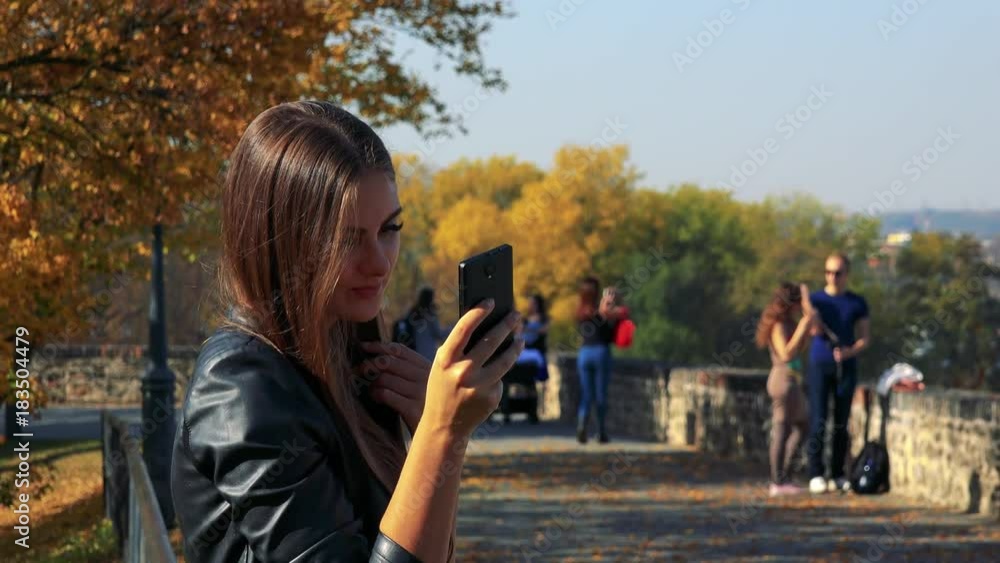 Young beautiful woman takes selfie photos in autumn park in sunny day Young beautiful woman takes selfie photos in autumn park in sunny day