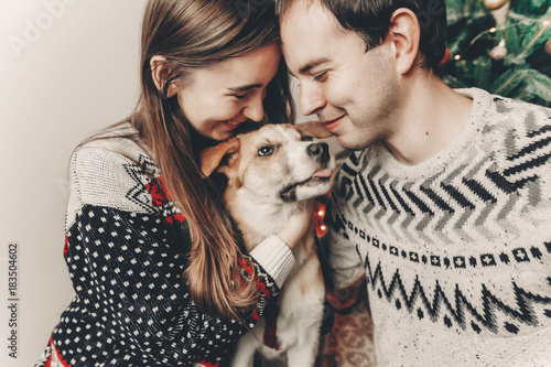 happy family in stylish sweaters having fun with cute dog in festive room with christmas tree. emotional moments. merry christmas and happy new year concept. happy holidays