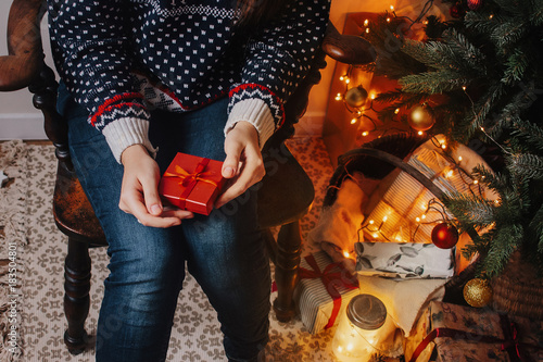 woman holding red gift and sitting at christmas tree in cozy evening. atmospheric moments. merry christmas and happy new year concept. happy holidays. christmas exchanging presents