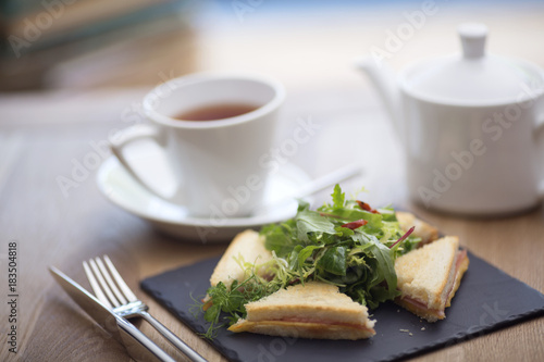 a variety of club sandwiches served in a white plate with a cup of hot tea