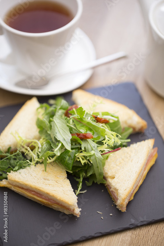 a variety of club sandwiches served in a white plate with a cup of hot tea