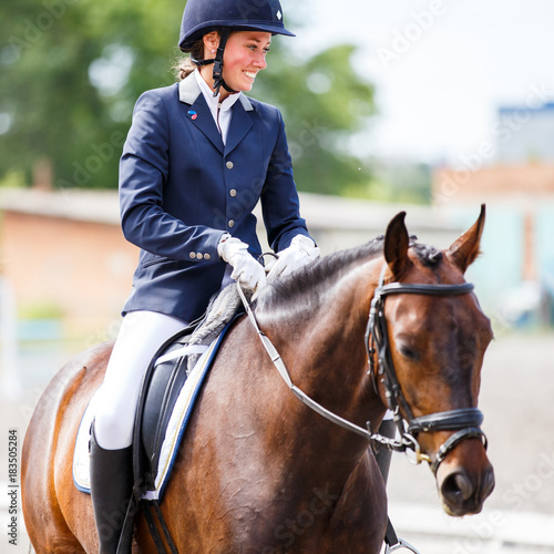 Young happy woman on her bay horse after dressage test on equestrian competitions