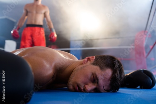 Canvas Print Unconscious male boxer lying by athlete in ring