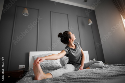 Healthy sporty shape middle aged woman doing seated yoga poses on the bed in the morning.