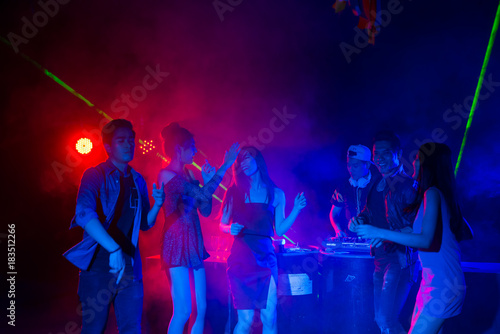 DJ playing music and Group of dancing friends enjoying night party. celebrating New Year together.