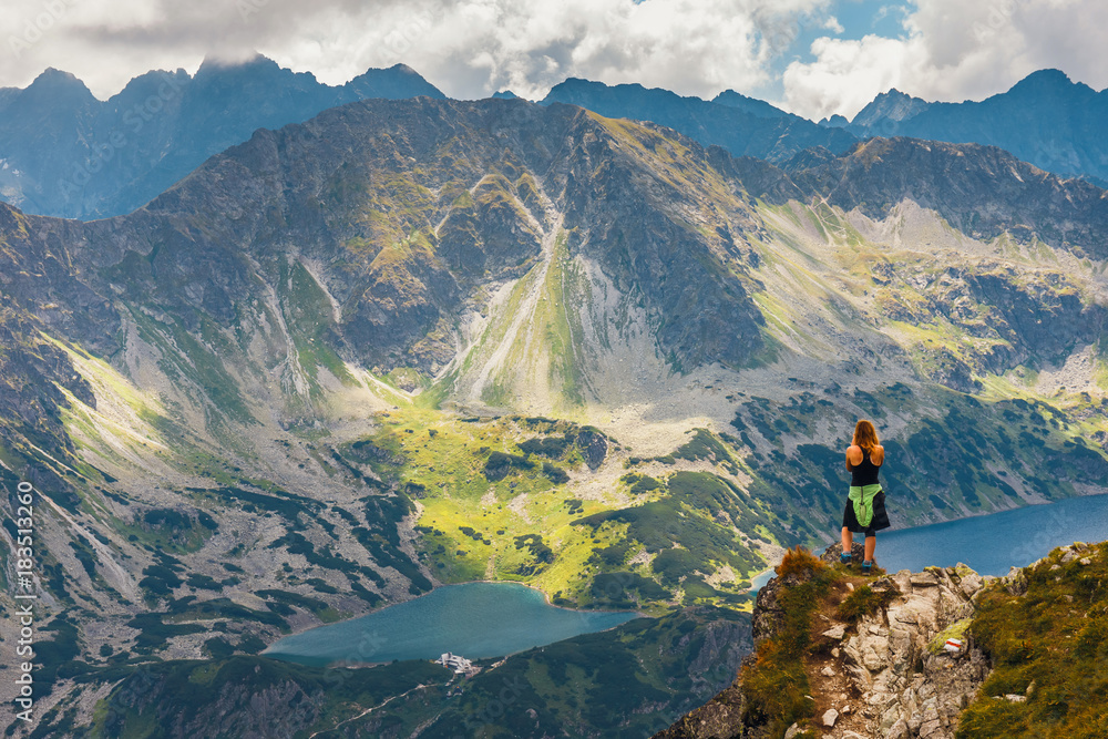 woman stands on the cliff and looks at the tops of mountains