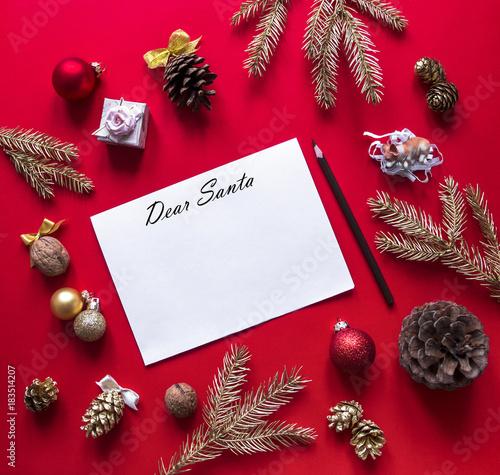 on a red raspberry background, New Year and Christmas decorations and spruce gold branches are arranged in a circle, and in the center lies a white sheet with a letter to Santa Claus and a pencil