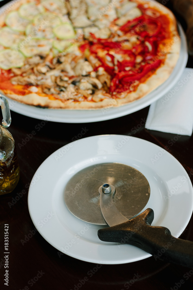 Pizza cutter on white plate. Round knife with pizza on background.