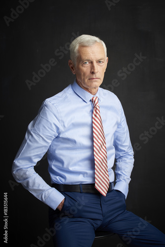 Elderly man portrait. An executive senior man wearing shirt and tie while sitting at isolated black background. 