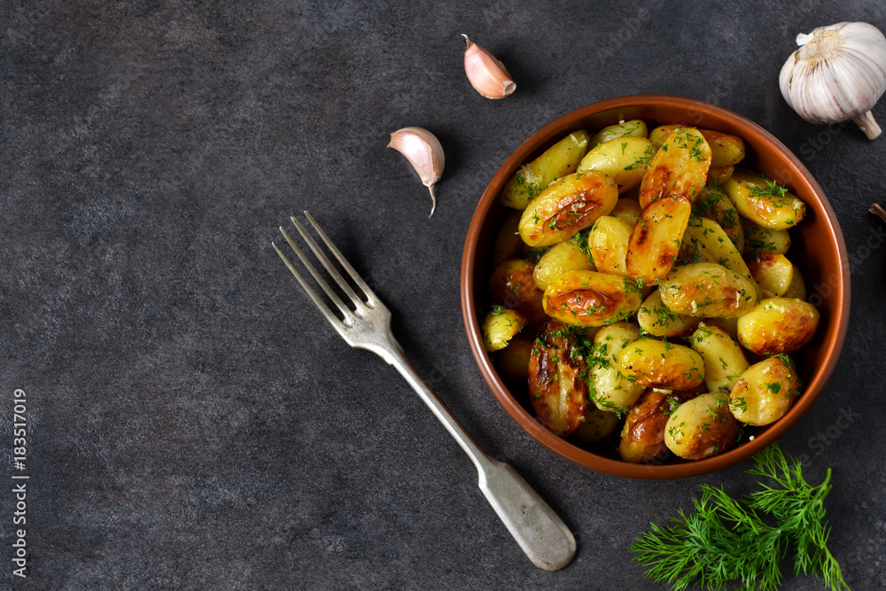 Young fried potatoes with garlic and dill on a black background