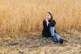 Portrait of a young brunette woman in black coat on a background of golden soybeans field, autumn outdoors